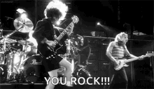 a black and white photo of a man playing a guitar on a stage with the words `` you rock '' written below him .