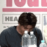 a man is sitting at a table with bottles of water in front of a sign that says heat .