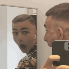 a man is taking a selfie in front of a mirror with his cell phone .