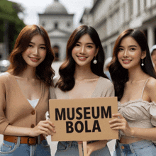 three women hold up a sign that says museum bola