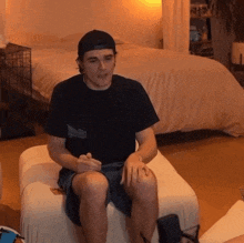 a man wearing a baseball cap is sitting on an ottoman in a bedroom .