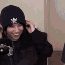 a man wearing a black beanie and a black jacket is smiling while talking on a cell phone .