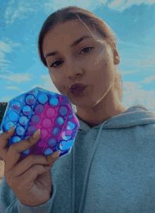 a woman blows a kiss while holding a purple and blue pop it