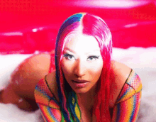 a woman with pink and blue hair is laying on her stomach in a bathtub .