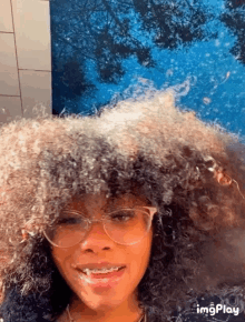 a woman with curly hair and glasses is smiling in front of a blue background .