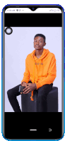 a young man in an orange hoodie is sitting on a black cube