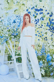 a woman in a white outfit stands in front of a wall of blue and white flowers