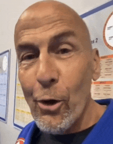 a bald man with a beard is making a funny face while wearing a blue karate uniform .