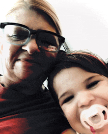 a woman with glasses holds a little girl with a pacifier