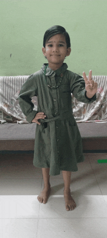 a little girl wearing a green dress is giving a peace sign