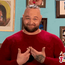 a man with a beard is wearing a red sweater and making a heart with his hands .