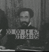 a black and white photo of a man with a beard sitting at a table with a timer on his face .