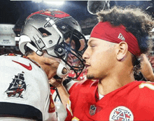 a man wearing a headband with the letter a on it looks at another man wearing a helmet