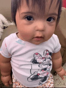 a baby is wearing a minnie mouse shirt and looking at the camera