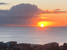 a sunset over the ocean with a cloud in the sky