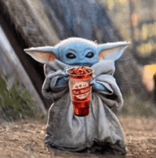 a baby yoda is holding a cup of strawberry iced tea .