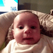 a baby is sitting in a high chair with a tv in the background