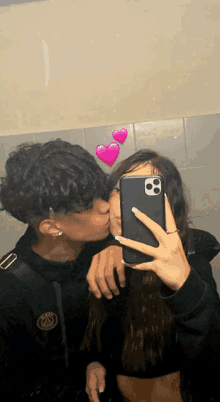 a man kisses a woman on the cheek while taking a selfie with his phone