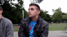 a man wearing a blue shirt with the letter j on it sits in a park