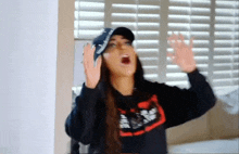 a woman wearing a baseball cap and a black sweatshirt is standing in front of shutters .