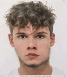 a young man with curly hair and a beard is standing in front of a white background .