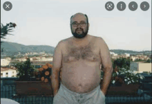 a shirtless man with glasses and a beard is standing on a balcony .