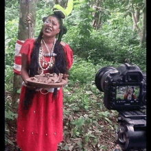 a woman in a red dress is standing in the woods holding a plate of food .