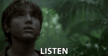 a young boy is standing in the jungle looking up at the sky and the word listen is visible in the foreground .