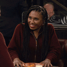 a woman with braids is smiling while sitting at a table with a plate of food in front of her