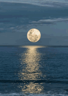 a full moon is rising over the ocean and is reflected in the water