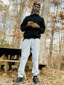 a man in a black sweater and grey sweatpants stands in the woods