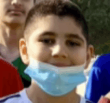 a young boy wearing a blue face mask is smiling in a crowd of people .