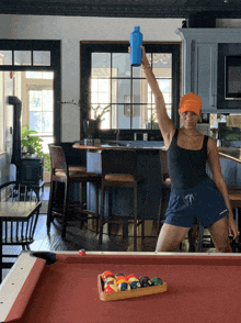 a woman standing in front of a pool table holding up a blue bottle