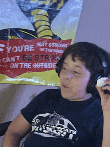 a boy wearing headphones in front of a poster that says you 're not strong