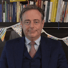 a man in a suit and tie stands in front of a shelf of books including one that says snom