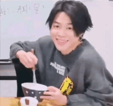 a young man is sitting at a table eating food from a bowl with a spoon .