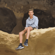 a boy in a hoodie sits on a rock in the desert