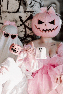 a woman in a pink dress with a pink pumpkin on her head is holding a ghost and a pumpkin .