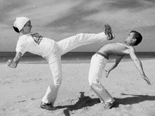 a man is kicking another man on the beach .