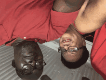 a man and a woman wearing red shirts and glasses are laying upside down