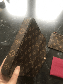 a person is holding a brown louis vuitton purse on a table