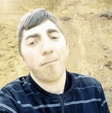 a man in a striped shirt is taking a selfie in front of a dirt hill .