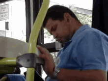 a man in a blue shirt is sleeping on a bus with a sign in the background that says praça de passageiros