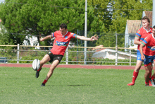 a rugby player wearing a red jersey with the word new york on it is kicking the ball