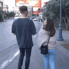 a man and a woman are walking down a sidewalk in front of a large billboard that says " t-mobile "