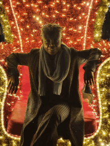 a man in a coat and scarf is sitting in a chair covered in lights