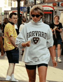 a woman wearing a harvard sweatshirt walking down a street