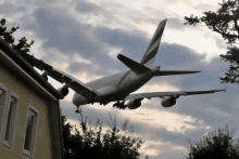 a large plane is flying over a building with trees in the foreground