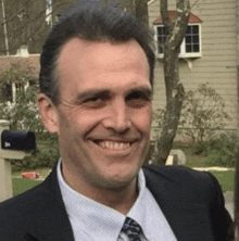 a man in a suit and tie is smiling in front of a mailbox that says 34