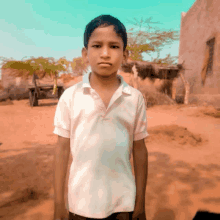 a young boy in a white shirt is standing in a dirt field